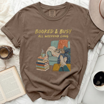 Brown t-shirt with "Booked & Busy All Weekend Long" text and cozy reading illustration.