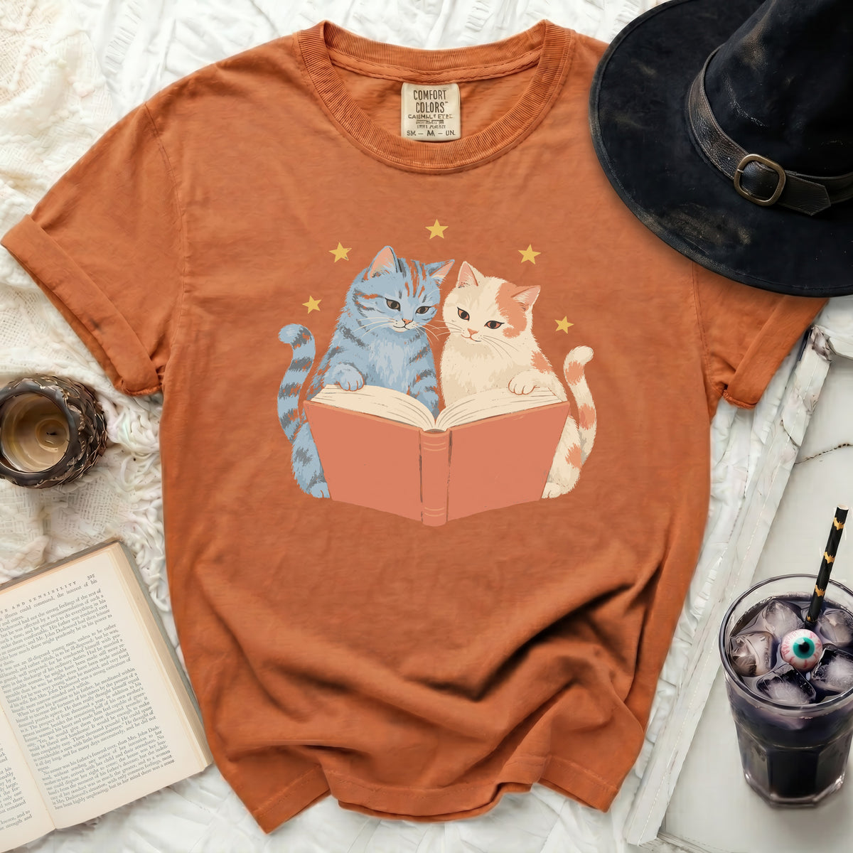 Orange t-shirt with two cats reading a book and stars graphic.
