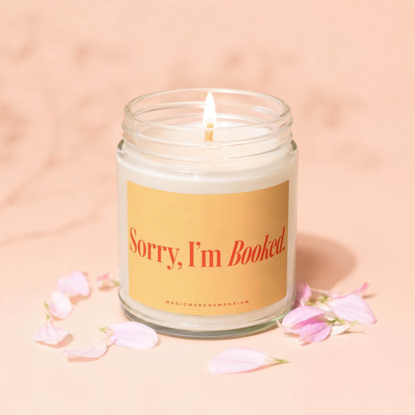 Glass jar candle with lit wick and text "Sorry, I'm Booked" surrounded by petals.