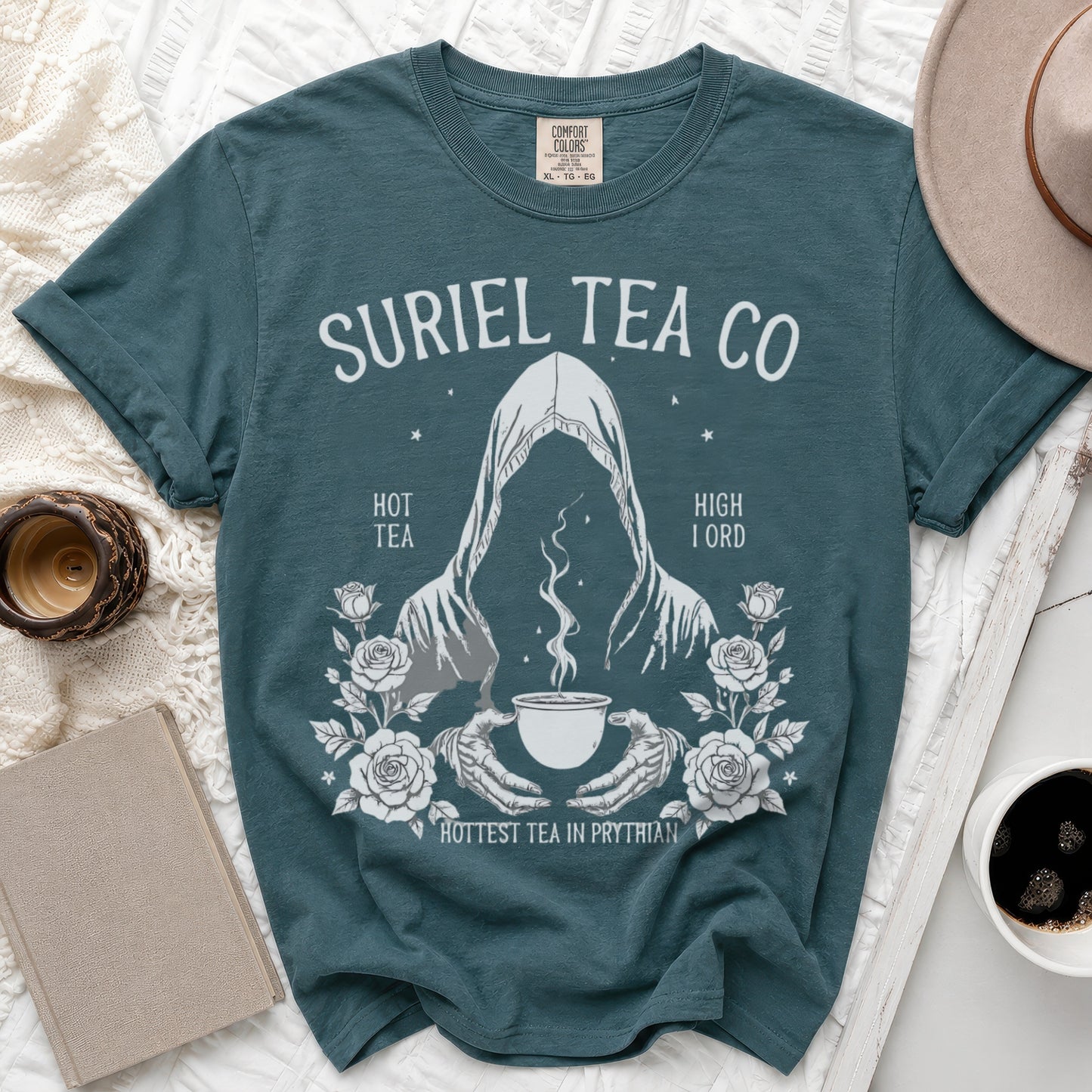 Teal t-shirt with "Suriel Tea Co" graphic featuring a cloaked figure, a cup of tea, and roses.