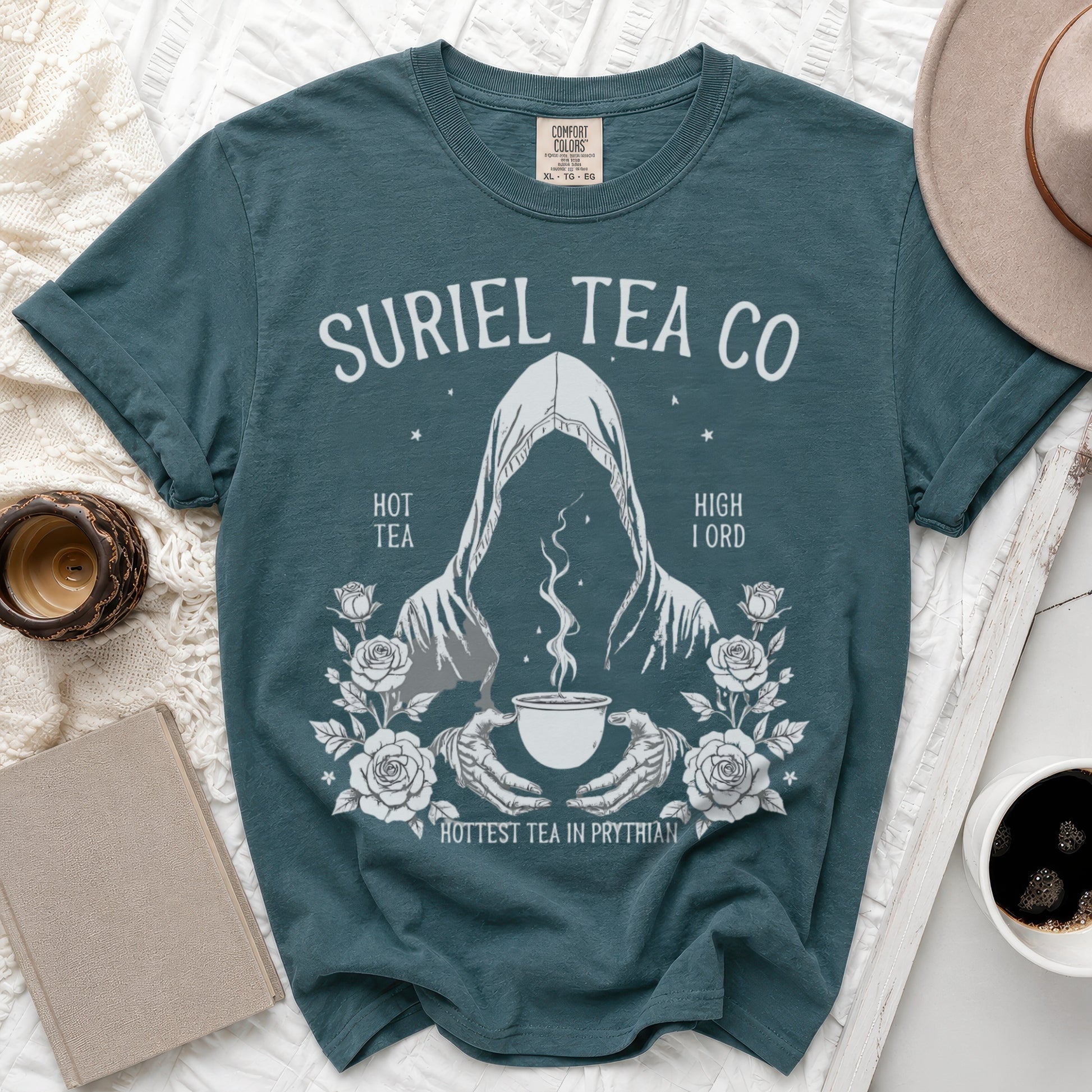 Teal t-shirt with "Suriel Tea Co" graphic featuring a cloaked figure, a cup of tea, and roses.