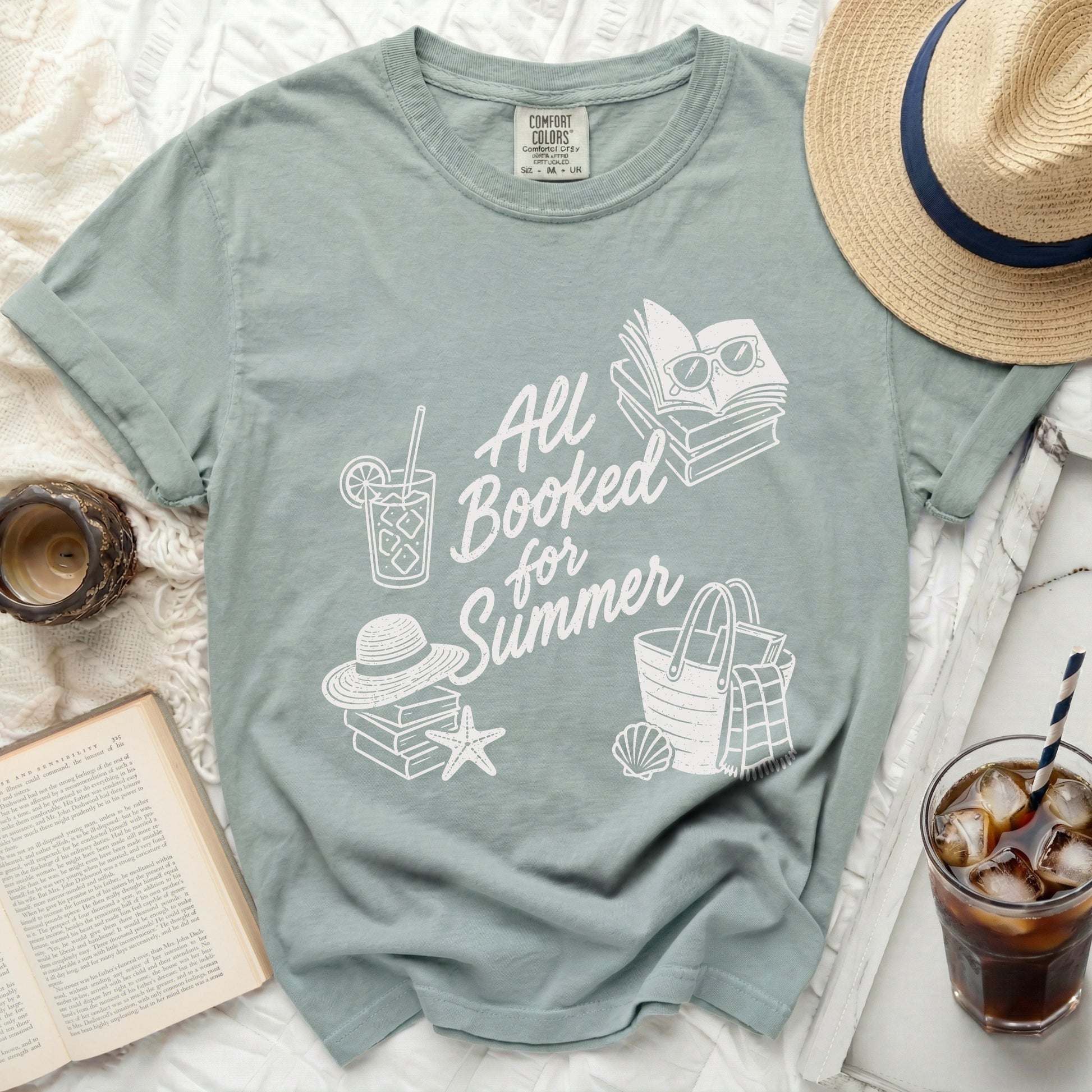 Dusty blue Comfort Colors t-shirt with stacked books, sunglasses, and beach items.