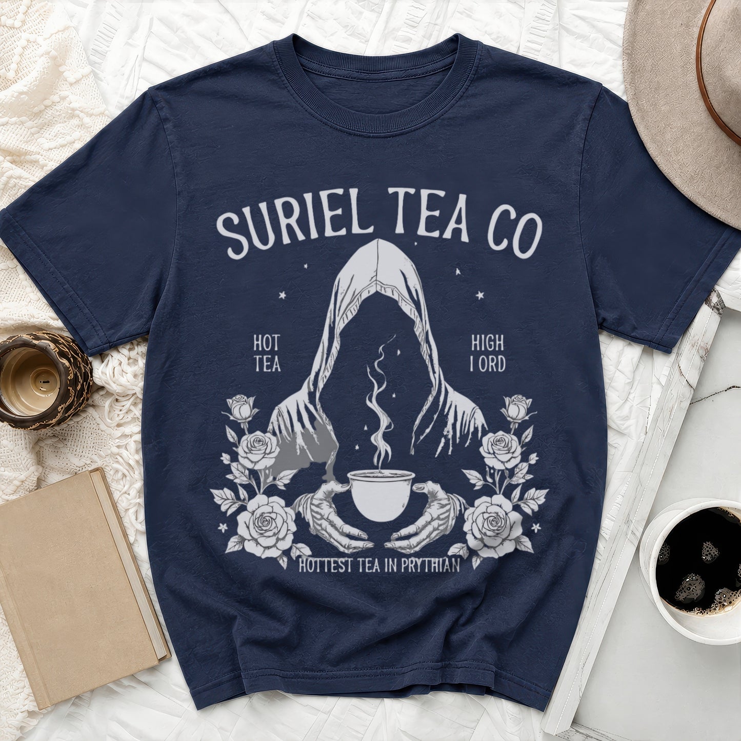 Navy t-shirt with "SURIEL TEA CO" logo featuring a hooded figure holding a teacup and roses.