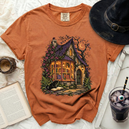 Orange t-shirt with Halloween cottage, black cat, and moon graphic.