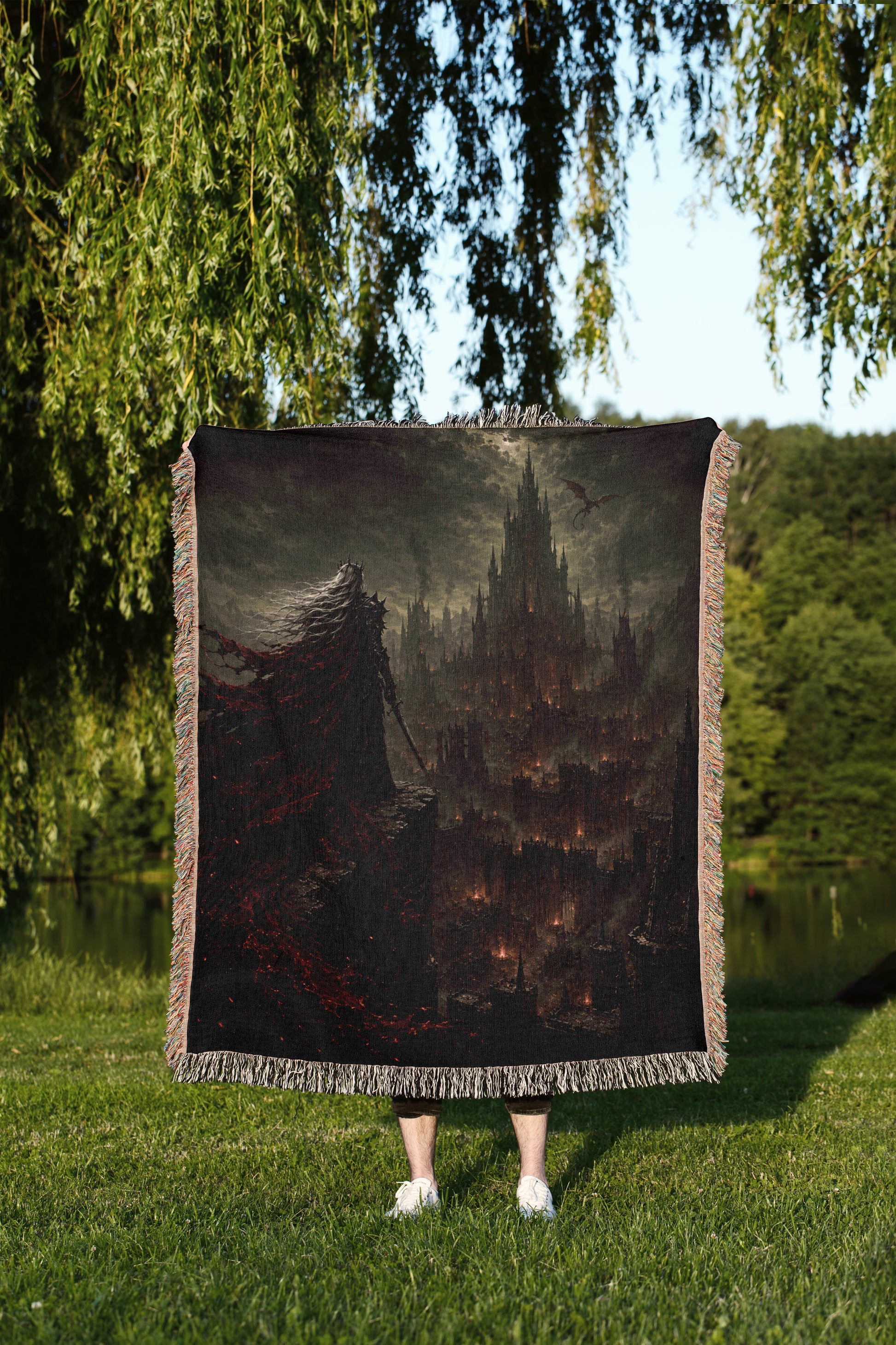 A person is standing in a grassy area, holding a large square blanket that features a dark, fantastical scene of a castle or cityscape.