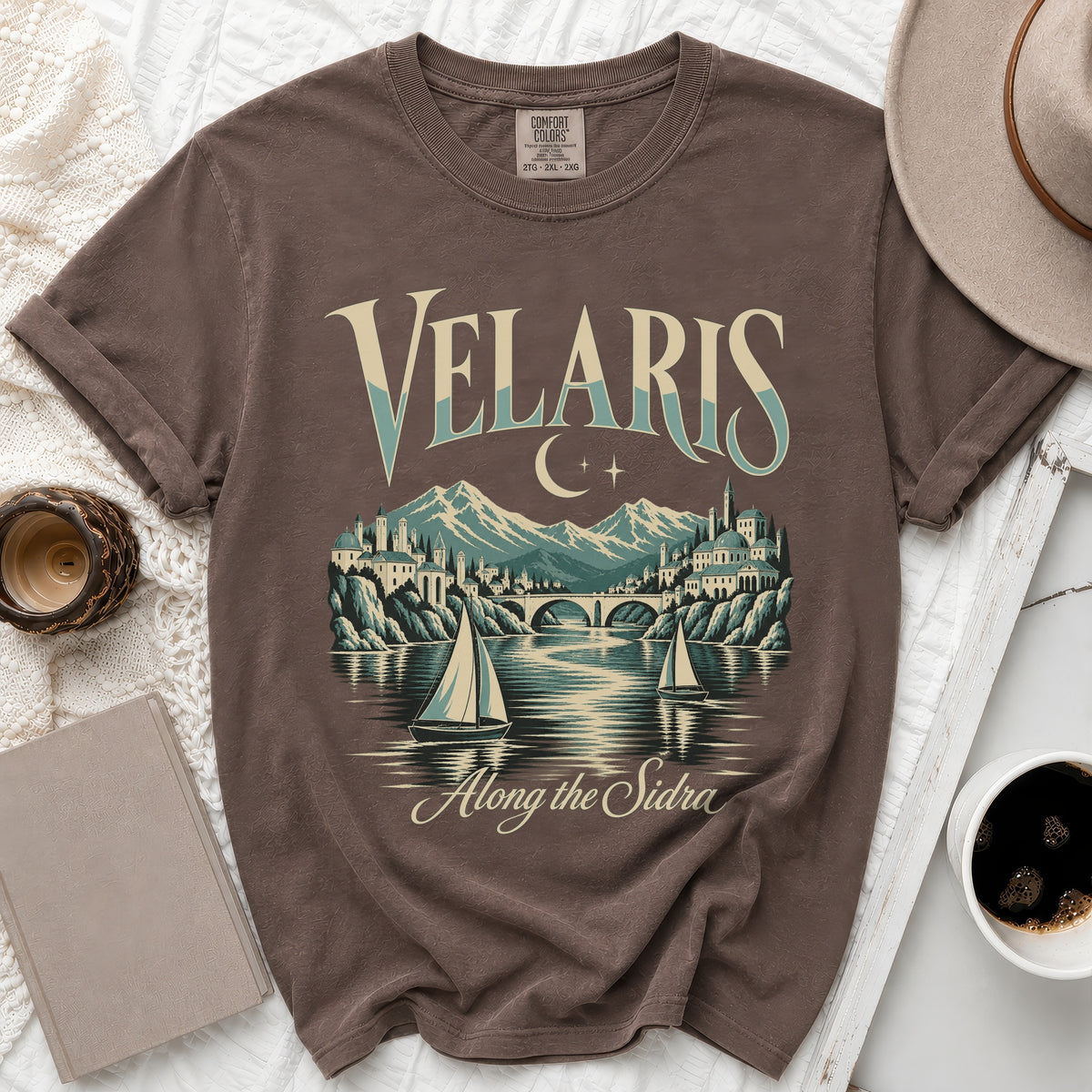 T-shirt graphic with "Velaris Along the Sidra" text, city, mountains, and sailboats.
