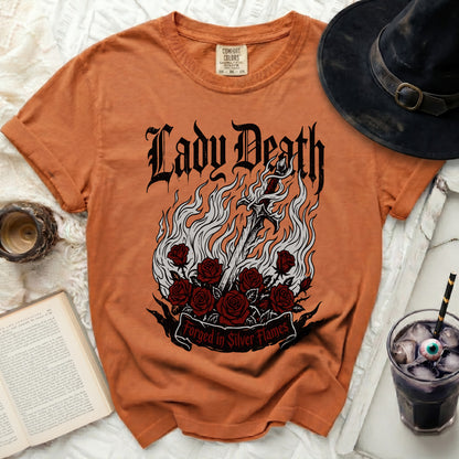 Orange t-shirt with Lady Death graphic, sword, roses, and "Forged in Silver Flames" text.