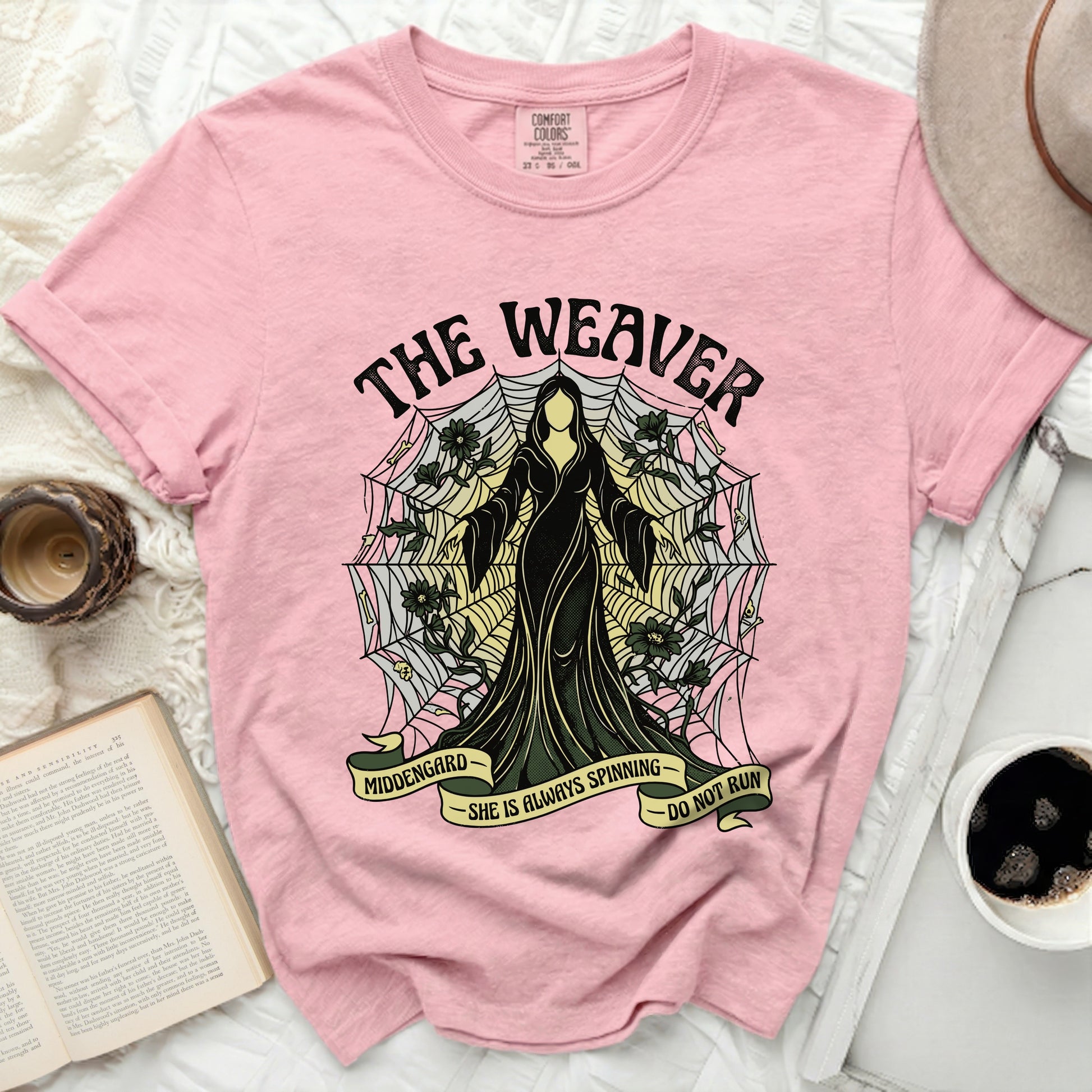 Pink t-shirt with "The Weaver" graphic and text "Middengard She Is Always Spinning Do Not Run".
