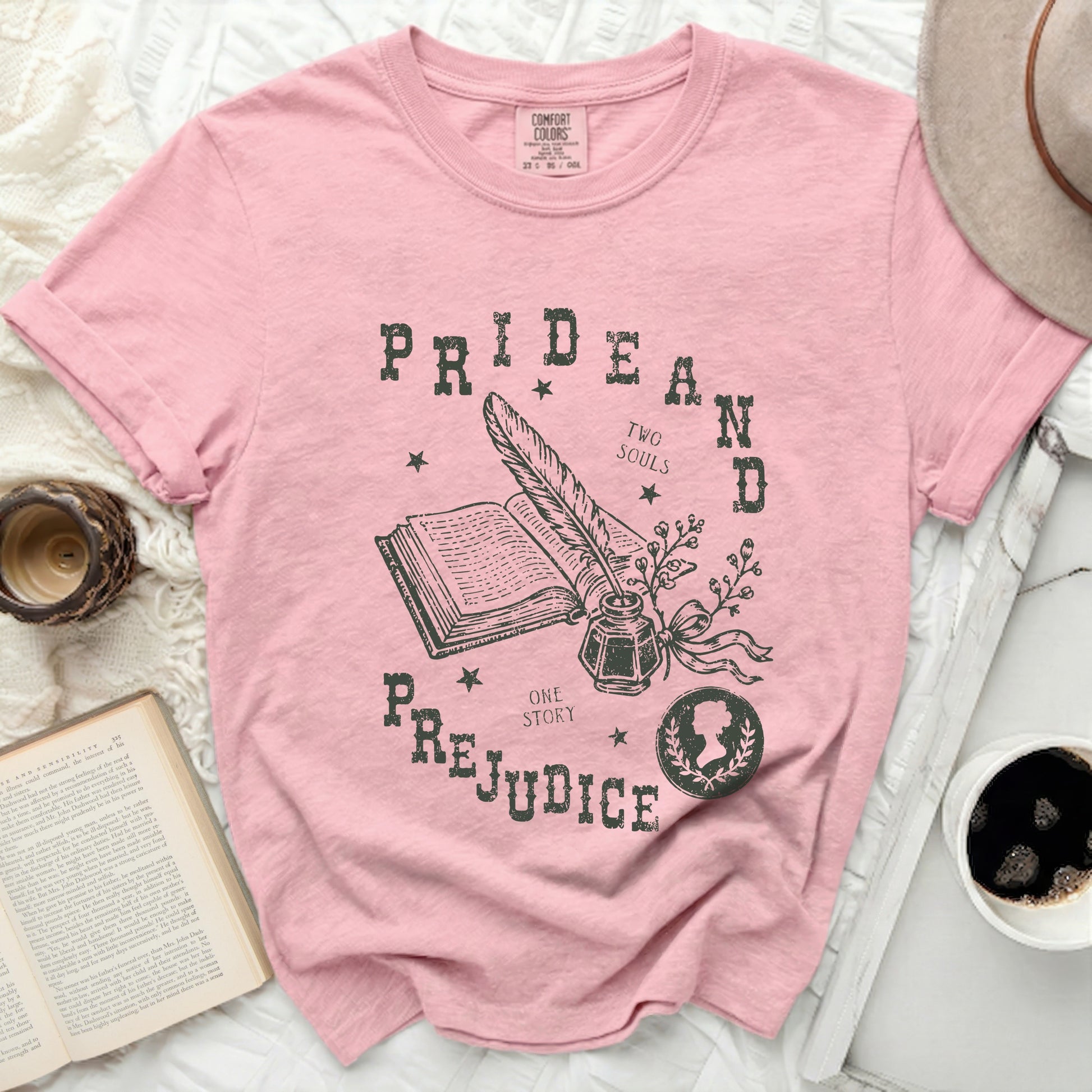 Pink t-shirt with a vintage-style graphic of an open book, quill, inkwell, and the words Pride and Prejudice.