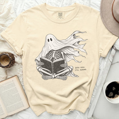Skeleton wearing a ghost costume reading a book with "DEAD TIRED. STILL READING." text.