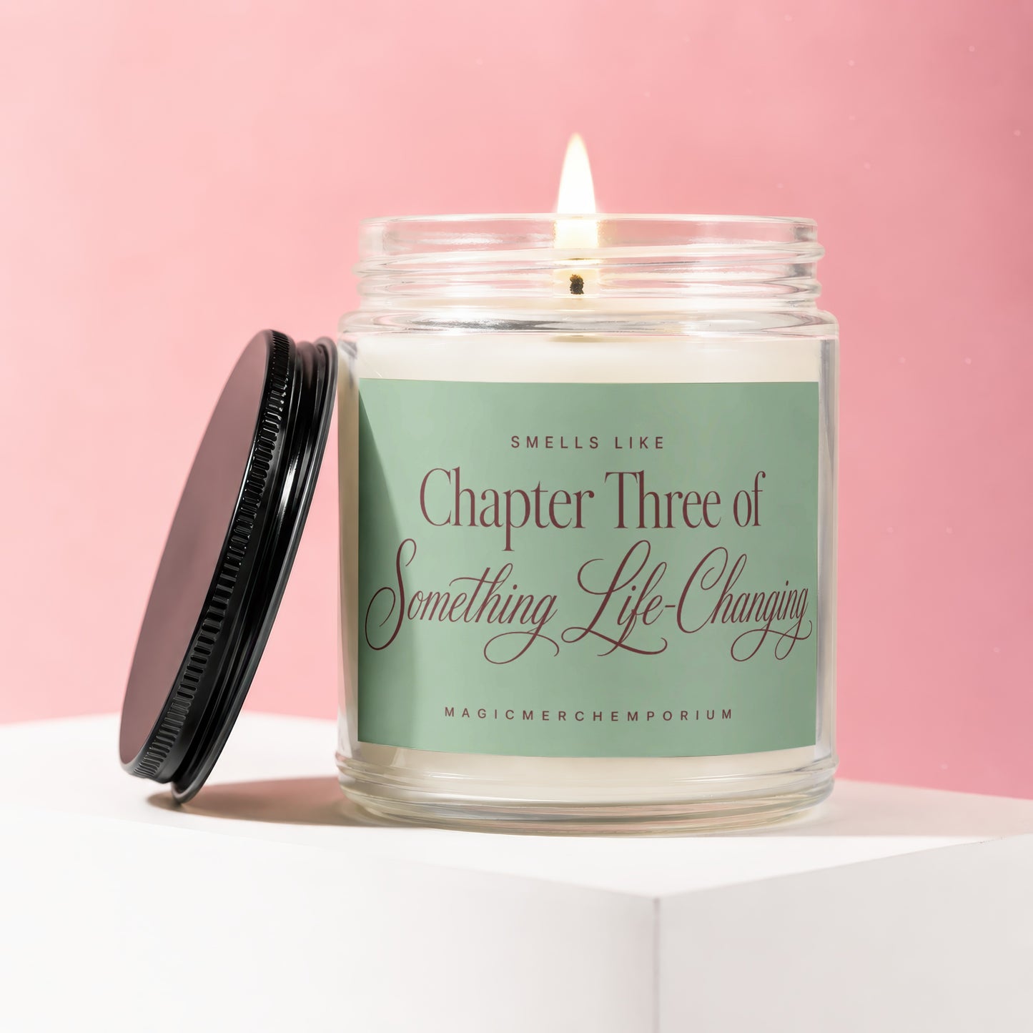 Lit candle in glass jar with black lid off to side, green label reads Chapter Three of Something Life-Changing.