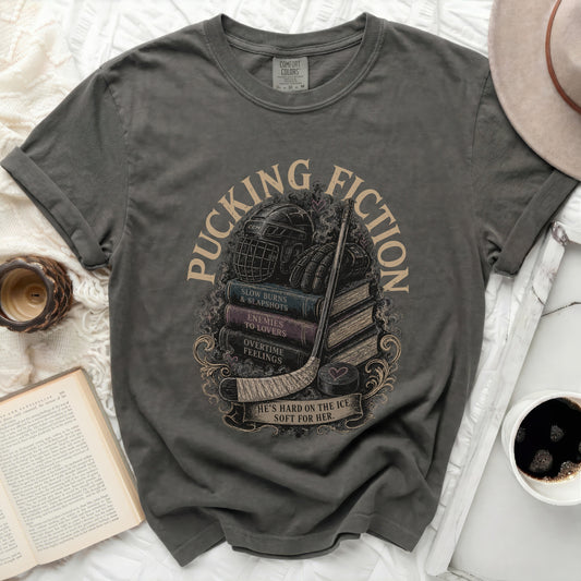 Dark gray t-shirt with stacked books, hockey gear, and "Pucking Fiction" text.