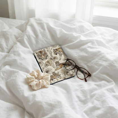 Journal with tiger and tropical leaf print, glasses, and scrunchie on white bedding.