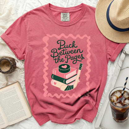 Pink t-shirt with "Puck Between the Pages" text, books, and hockey stick graphic.