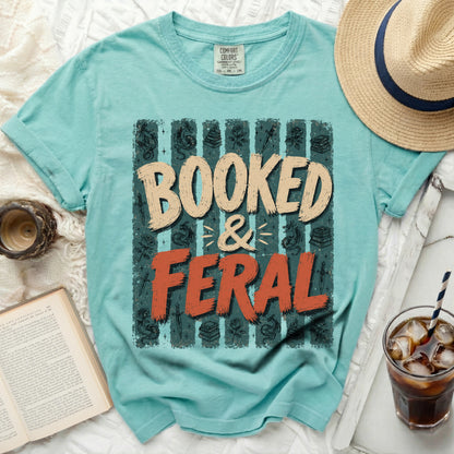 Teal t-shirt with "BOOKED & FERAL" graphic and book-themed illustrations.