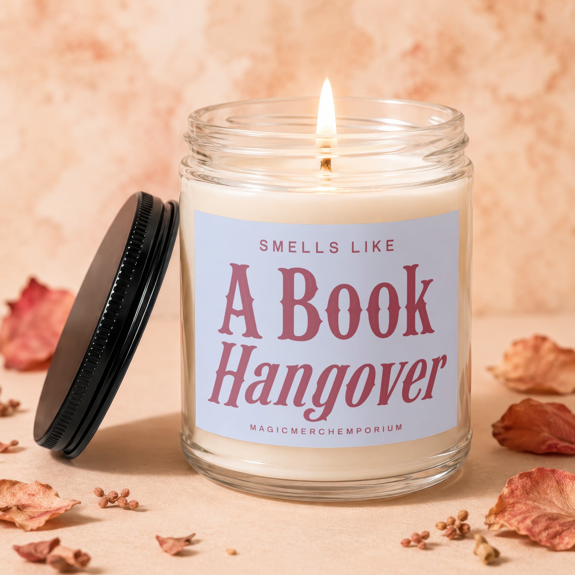 Lit candle in a glass jar with a black lid, labeled "Smells Like A Book Hangover".