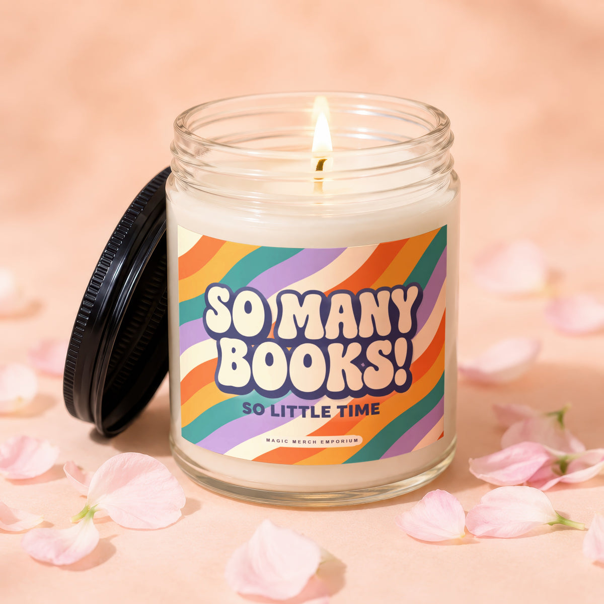 A lit candle in a glass jar with a colorful label that reads SO MANY BOOKS!
