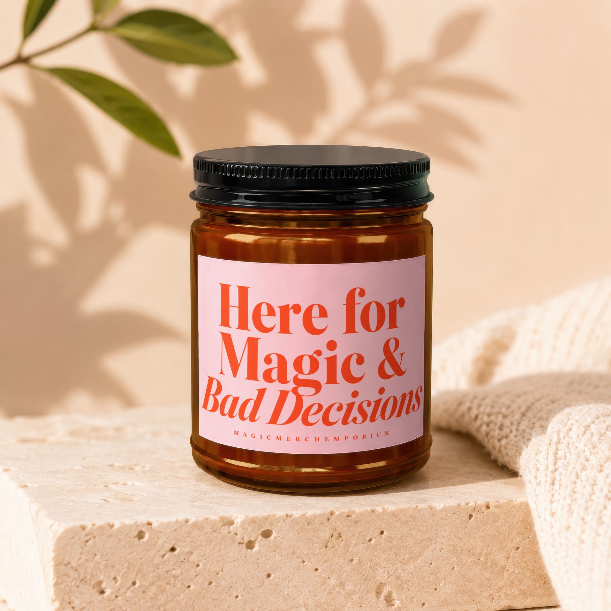 Amber candle with pink label reading "Here for Magic & Bad Decisions."