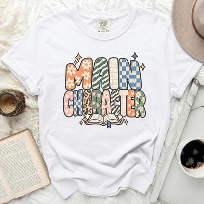 White t-shirt with "MAIN CHARACTER" graphic featuring retro patterns and an open book.