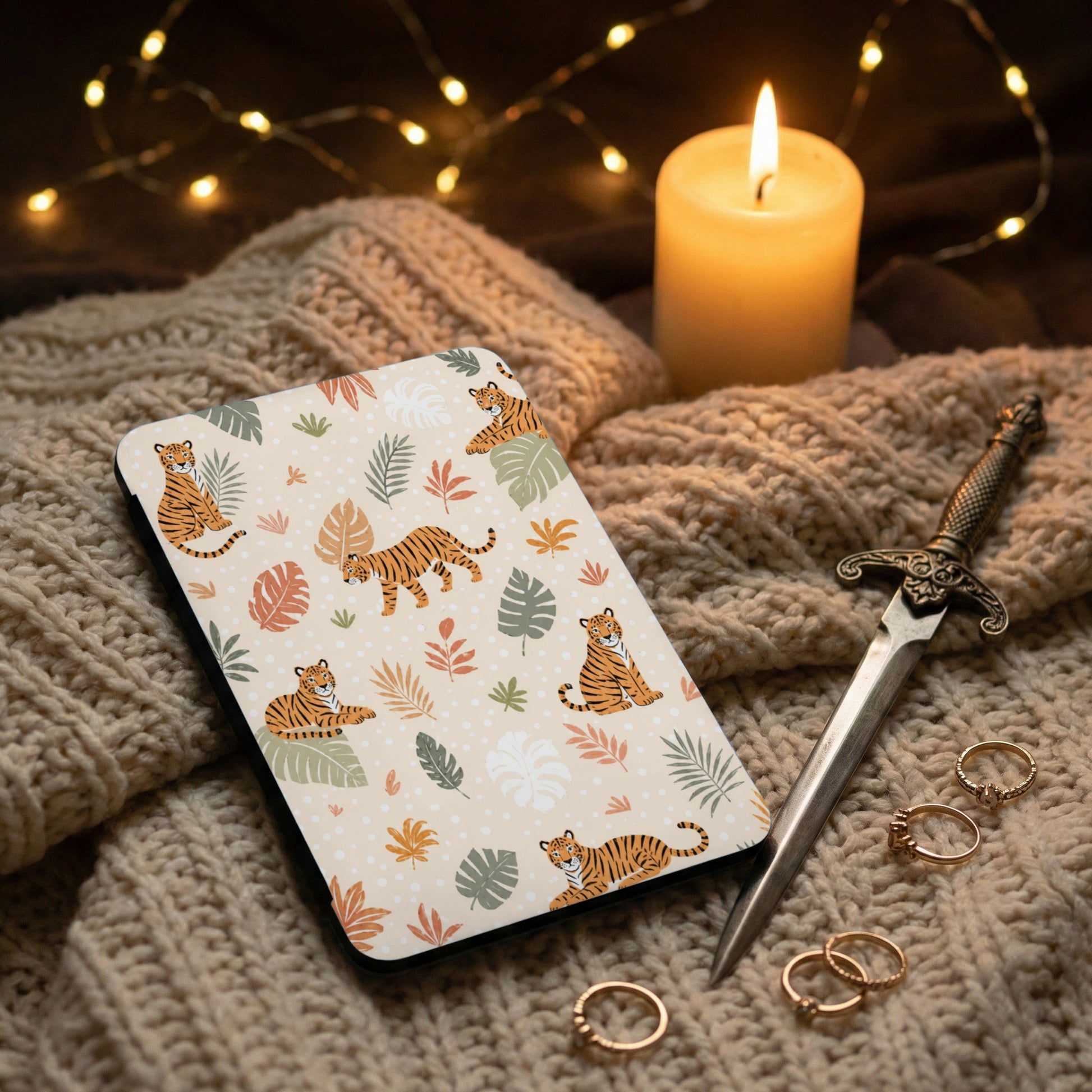 Book cover with tiger and leaf pattern on textured fabric next to candle and rings.