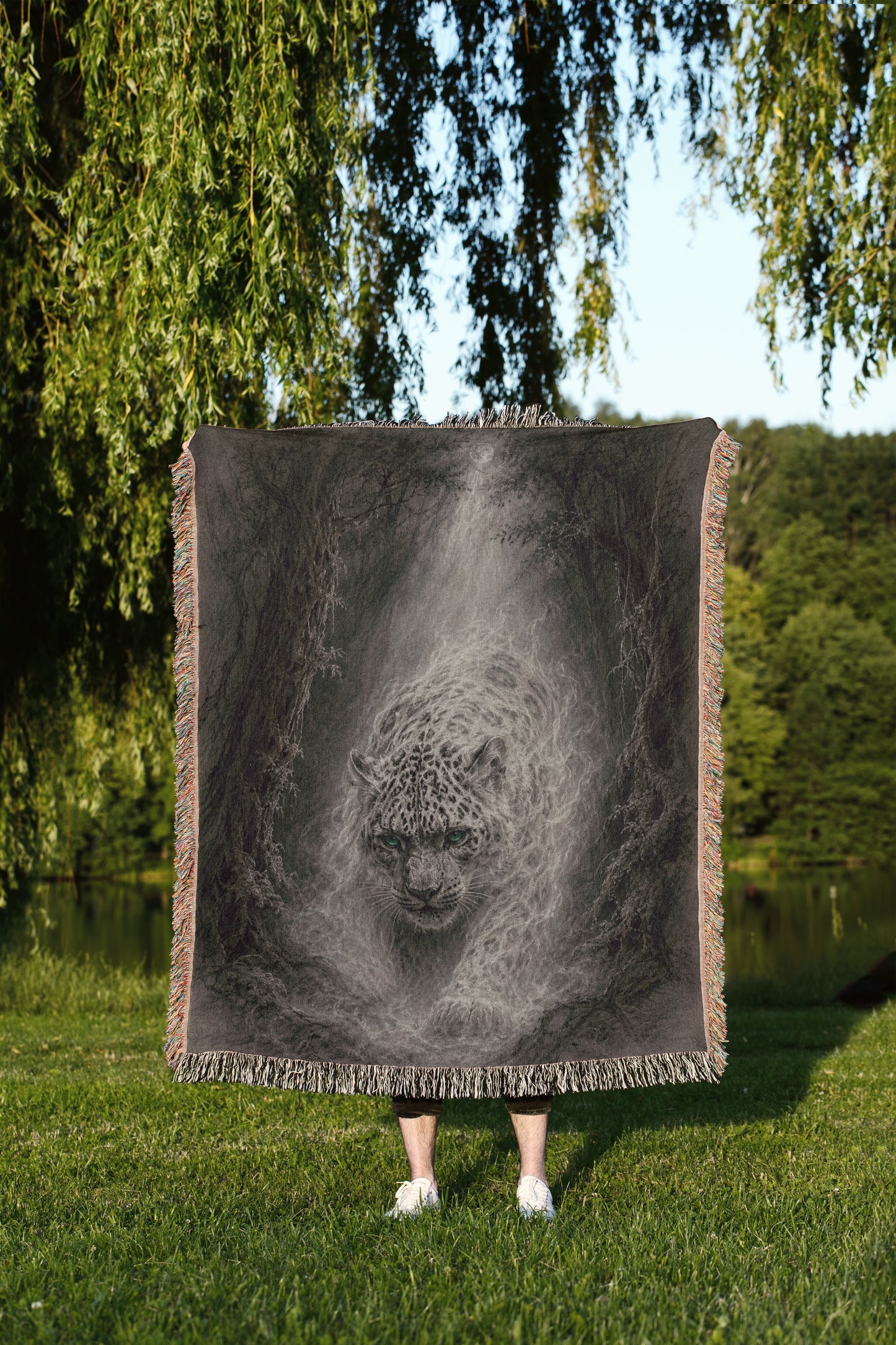 A person is standing in a grassy area, holding a large square blanket that features a striking black and white image of a leopard.