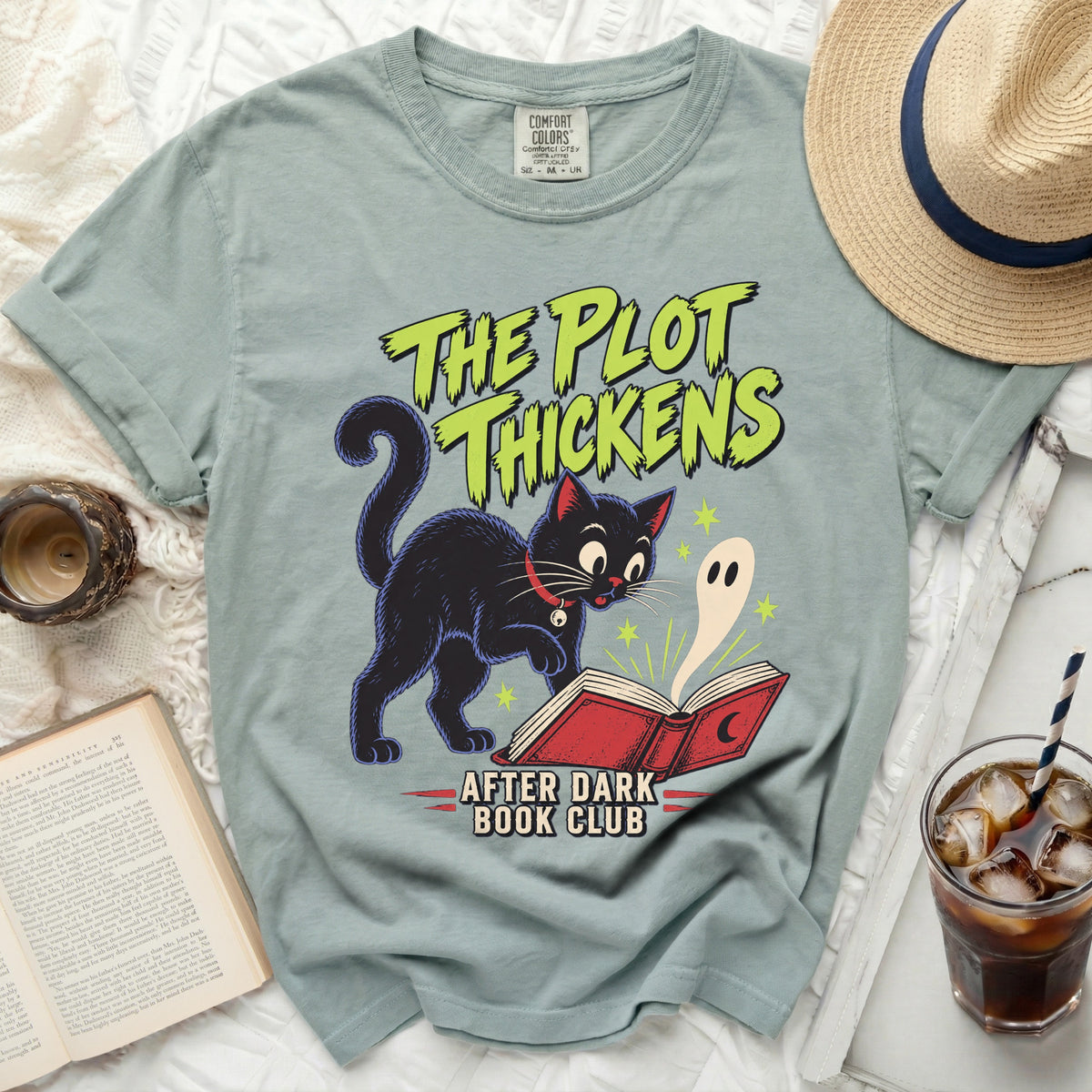 Light blue t-shirt with a black cat, ghost, and "The Plot Thickens After Dark Book Club" graphic.
