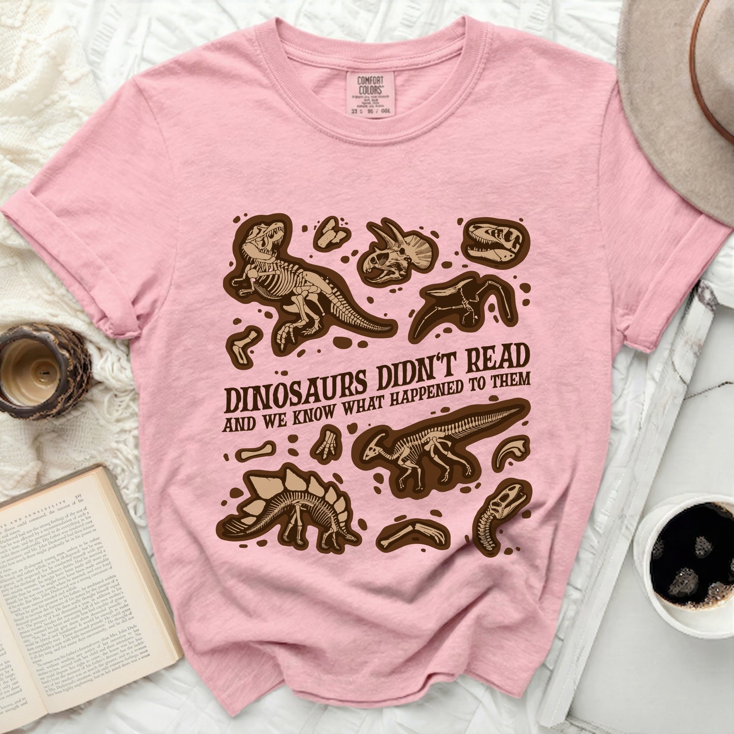 Pink t-shirt with brown dinosaur skeletons and text "DINOSAURS DIDN'T READ".