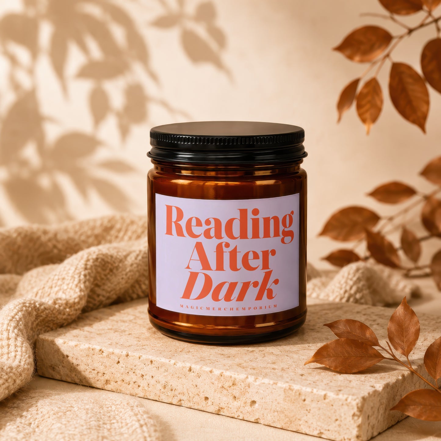Amber glass candle with "Reading After Dark" label, on textured stone with draped fabric.