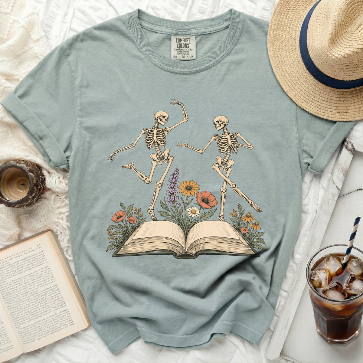 Two skeletons dance on an open book surrounded by flowers.