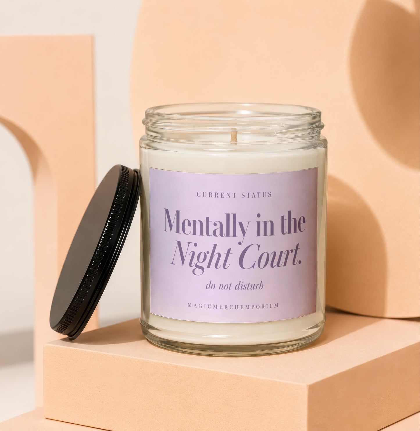 A scented candle in a glass jar with a purple label resting on a peach platform.