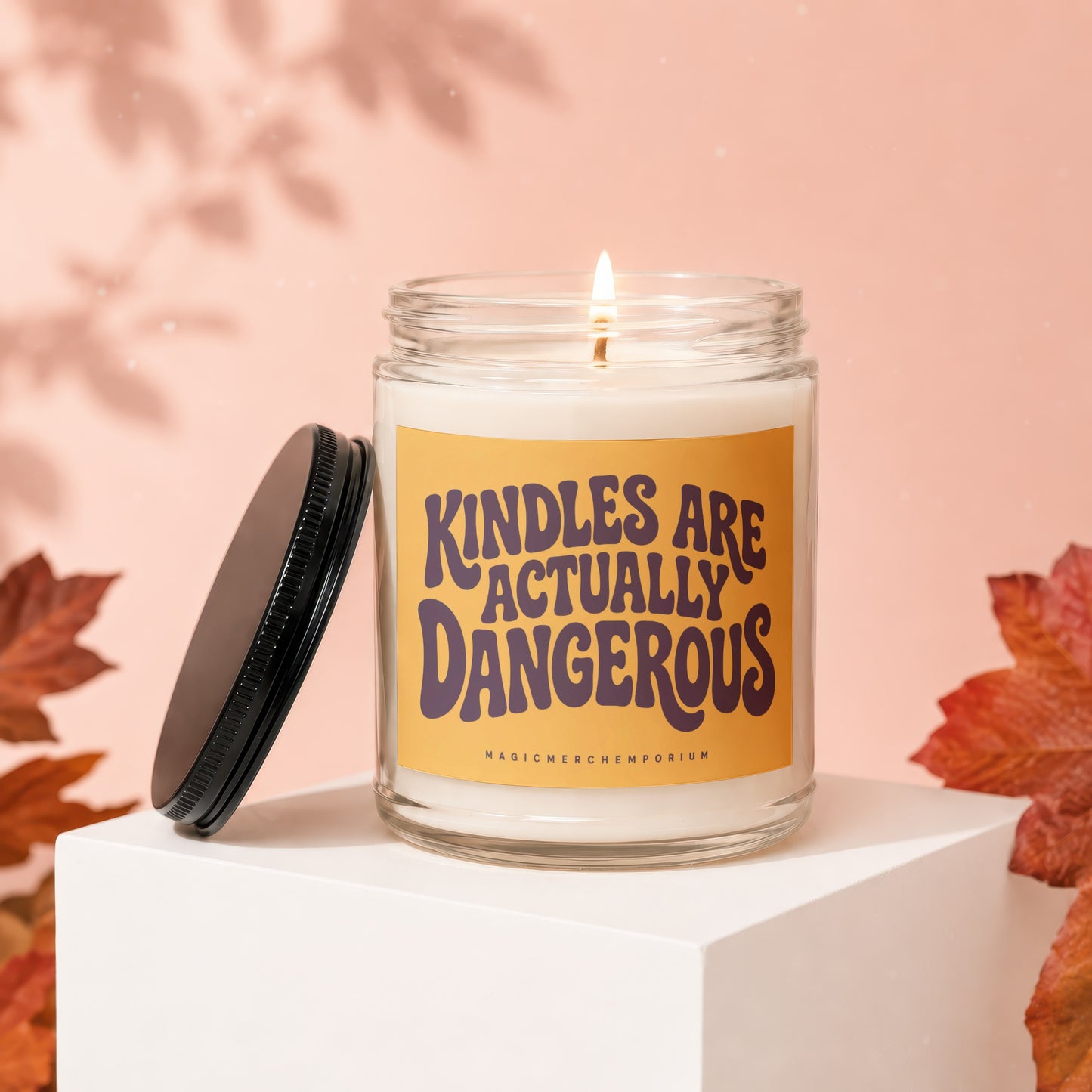 Candle with "Kindles Are Actually Dangerous" text, lid askew, on a pedestal.