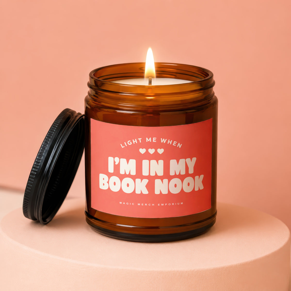 Amber jar candle with a lit wick and a coral label that says "I'm in my book nook."