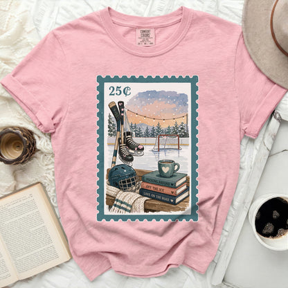 Pink t-shirt with postage stamp graphic featuring ice skates, hockey sticks, and a mug.