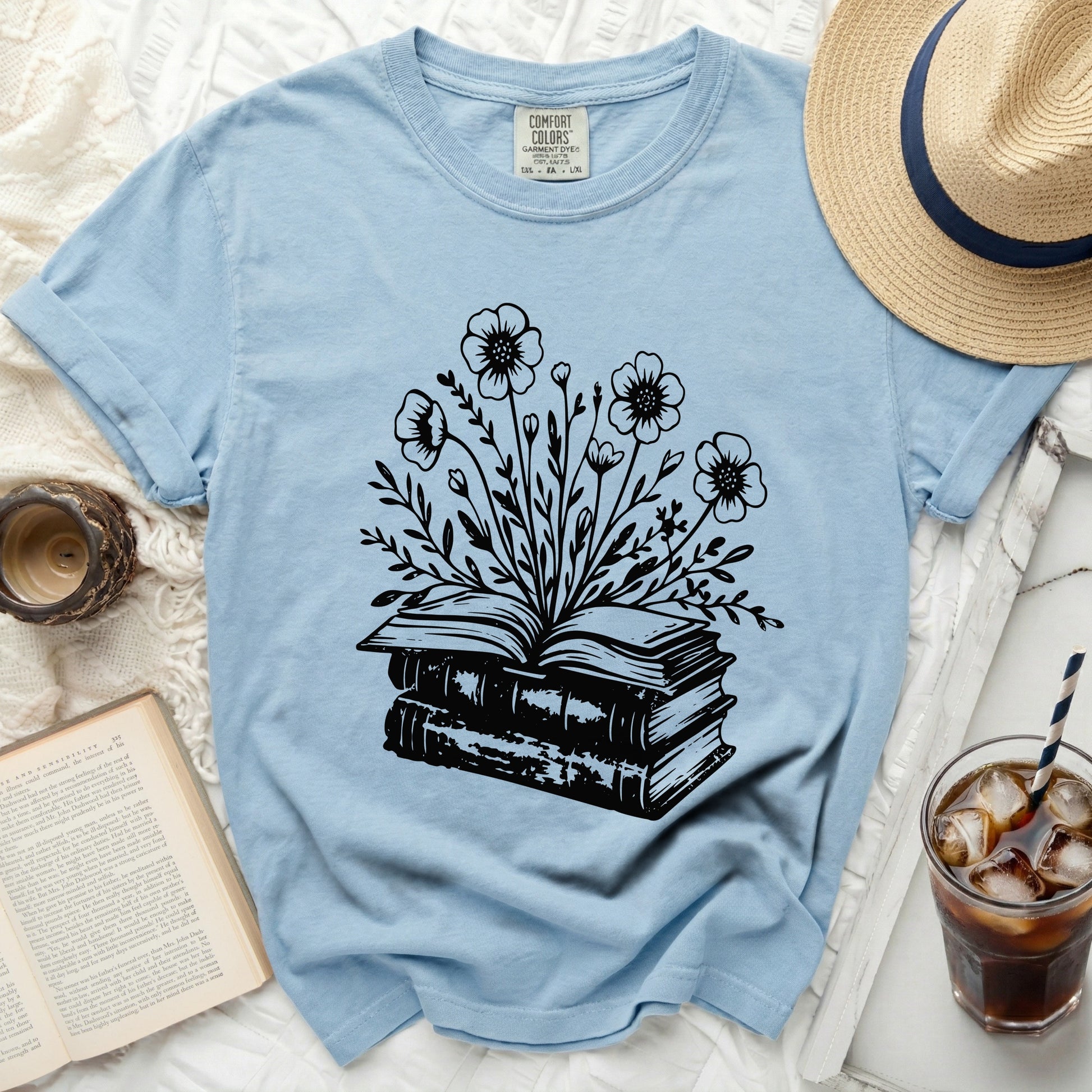 Light blue t-shirt with black line drawing of flowers blooming from stacked books.