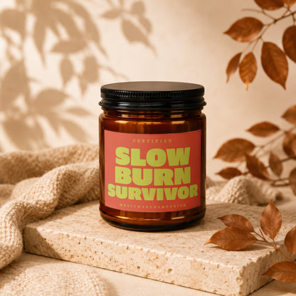Brown candle jar with "SLOW BURN SURVIVOR" text on a coral label.