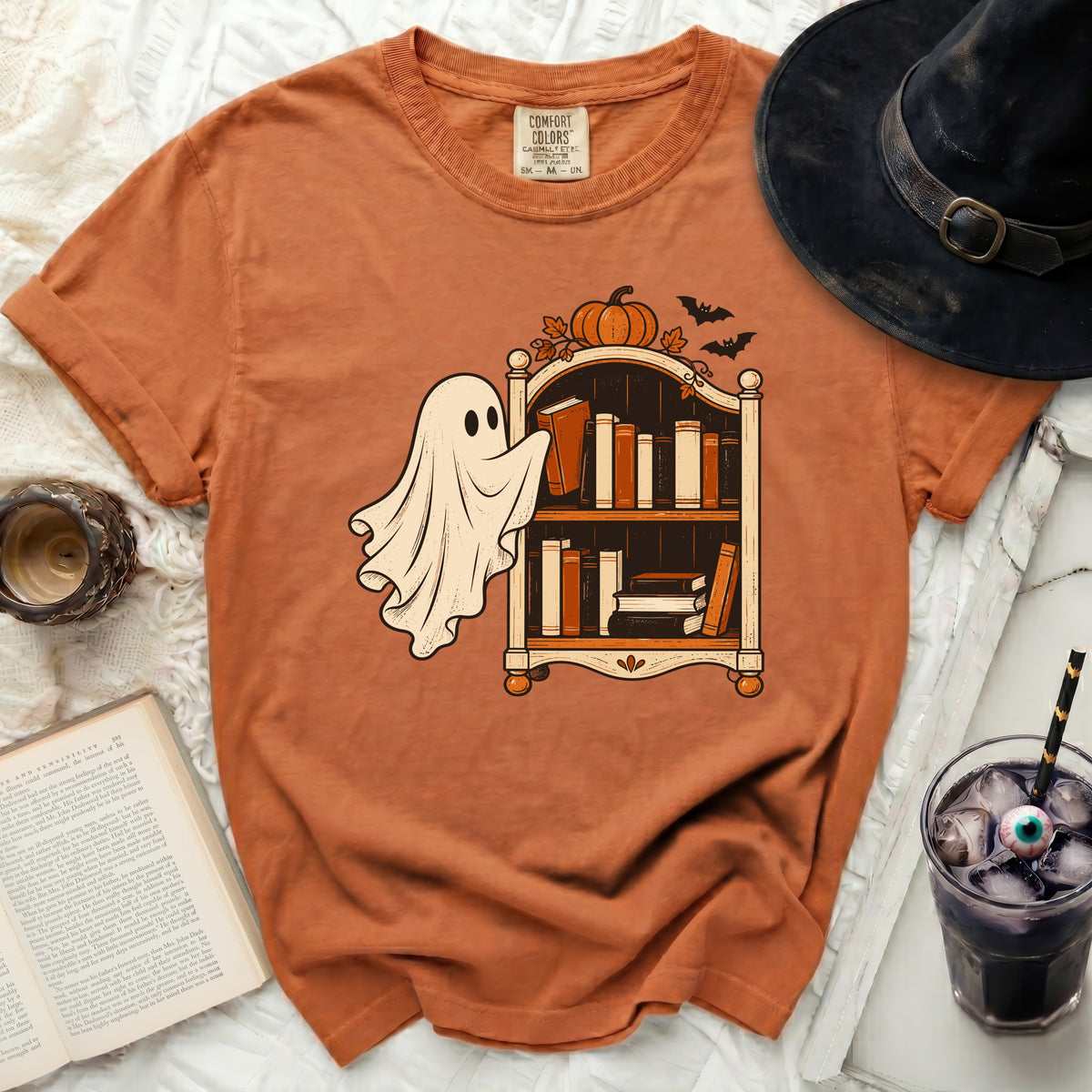 Orange t-shirt with a ghost reaching for books on a shelf with pumpkin and bats.