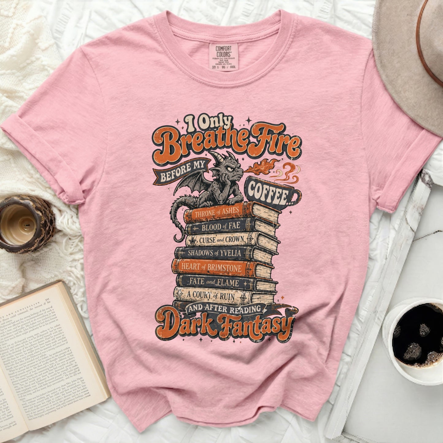 Pink t-shirt with "I Only Breathe Fire Before My Coffee" and dark fantasy book titles.