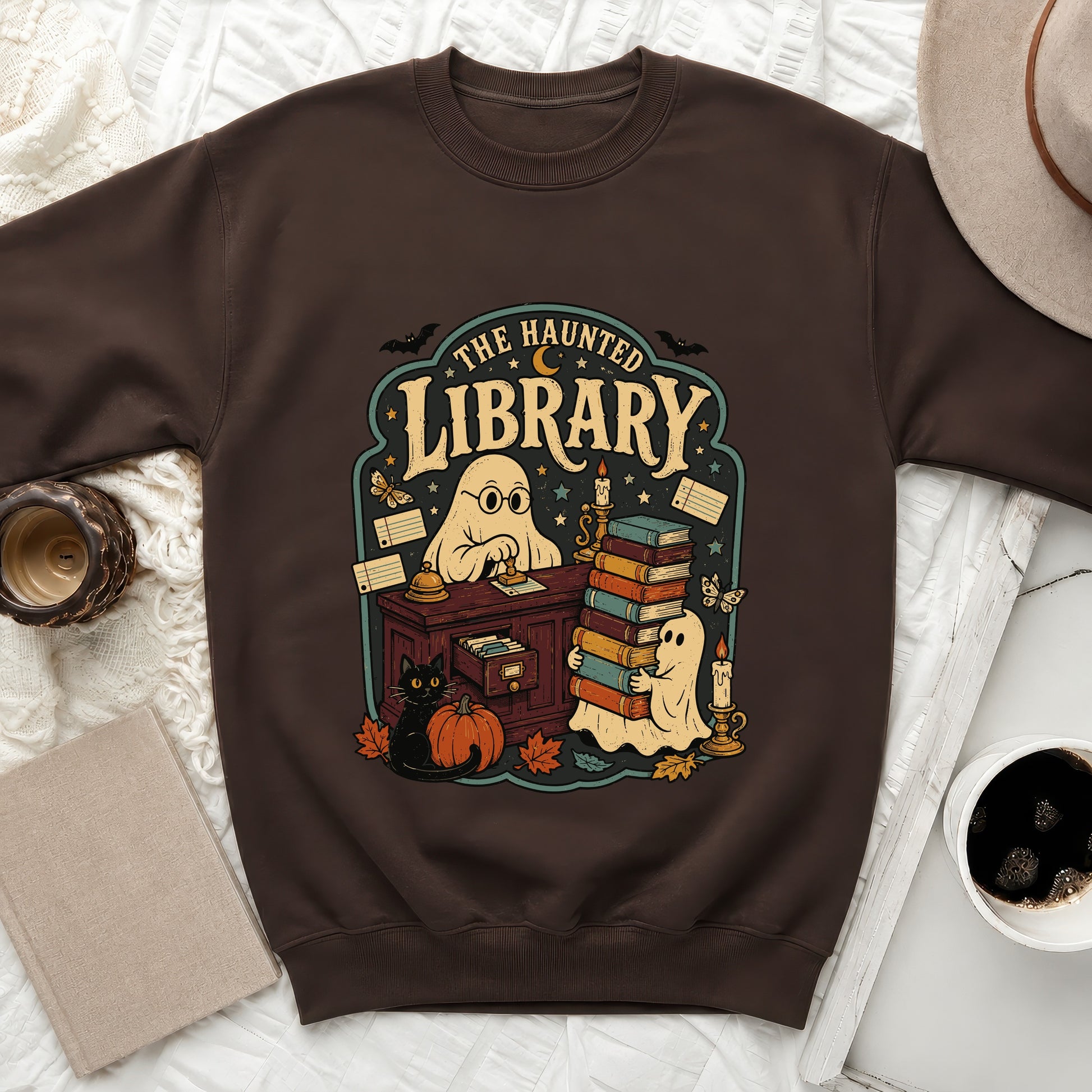 Brown sweatshirt with "The Haunted Library" ghost, cat, pumpkin, and books graphic.