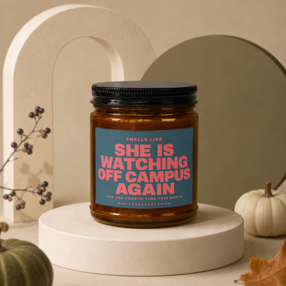 Amber candle with blue label that reads "She Is Watching Off Campus Again".