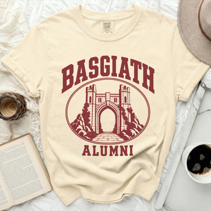 A cream crewneck t-shirt featuring a maroon collegiate-style design with the text "Basgiath Alumni" and a stone gateway.