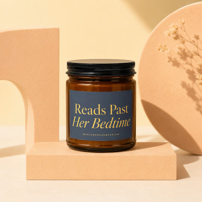 Amber glass candle with black lid and dark blue label reading "Reads Past Her Bedtime".
