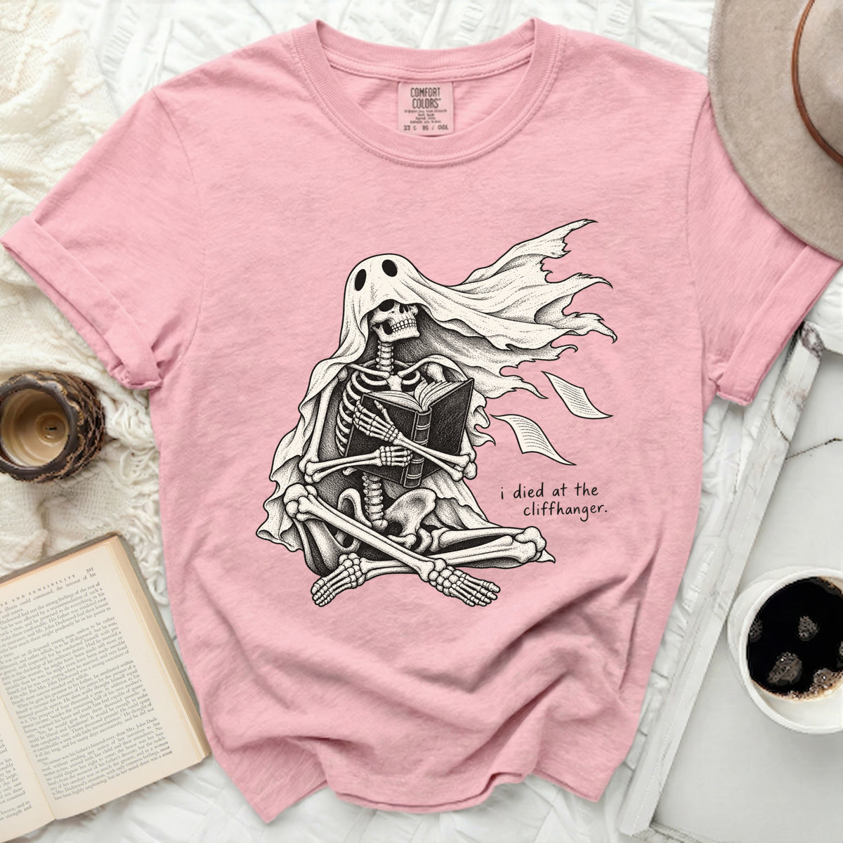 Skeleton in a ghost costume reading a book with text "i died at the cliffhanger."