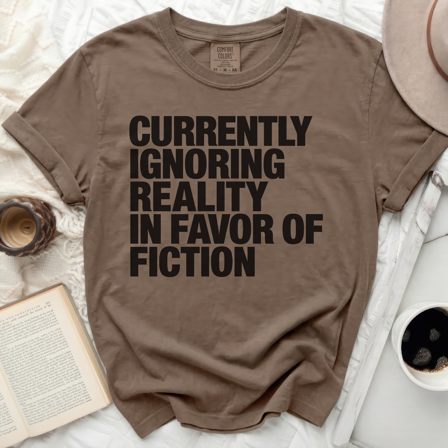 T-shirt with black text reading "Currently Ignoring Reality In Favor of Fiction."