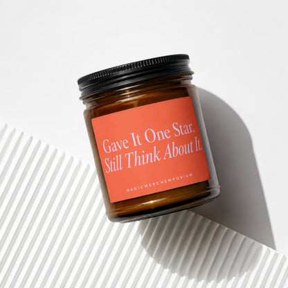 Amber candle jar with black lid on orange label reading "Gave It One Star. Still Think About It."
