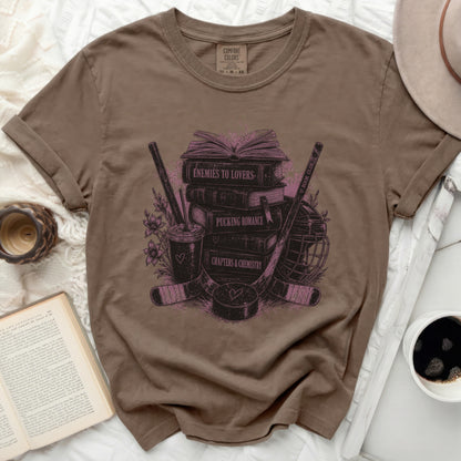 Brown t-shirt with books, hockey gear, and "Enemies to Lovers" text graphic.