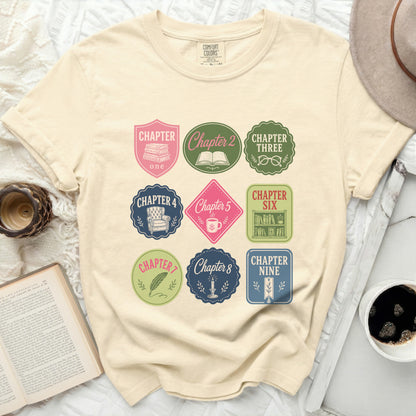 Cream t-shirt with nine embroidered book chapter badges.