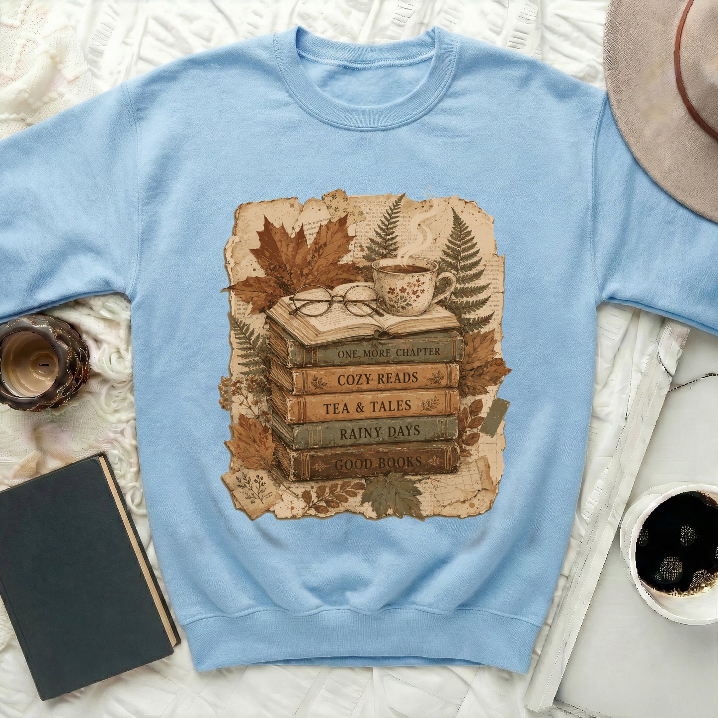 Light blue sweatshirt with a graphic of books, glasses, tea, and autumn leaves.