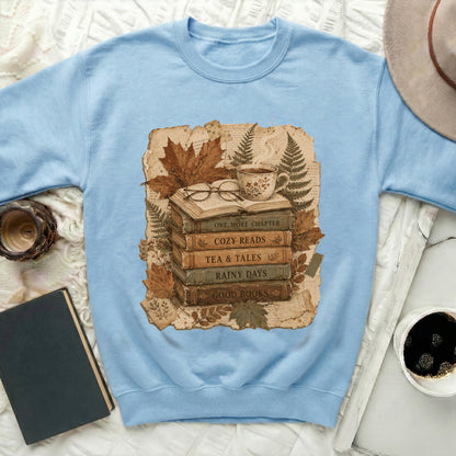 Light blue sweatshirt with a graphic of books, glasses, tea, and autumn leaves.