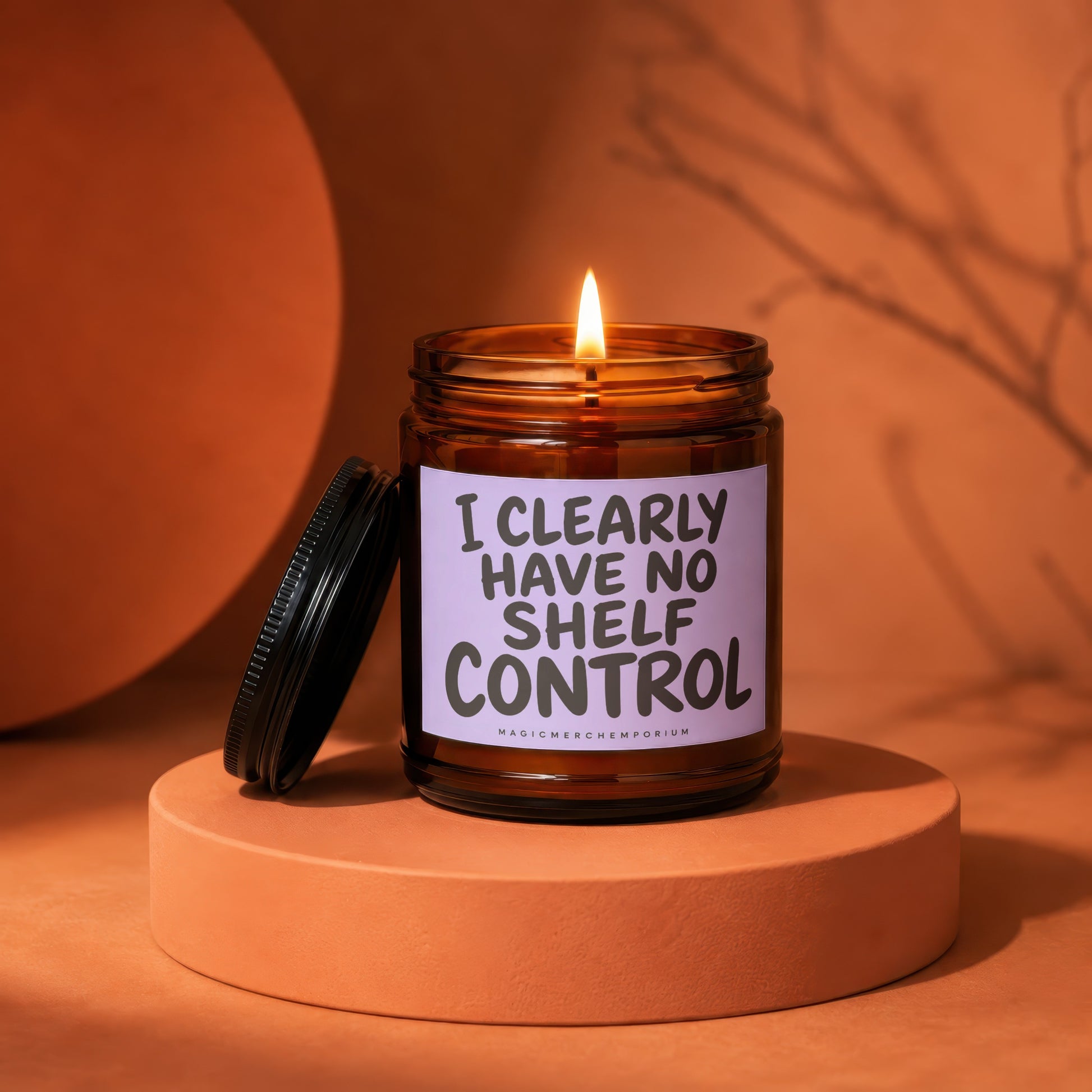 Amber candle with lit flame, label reads "I CLEARLY HAVE NO SHELF CONTROL".