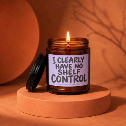 Amber candle with lit flame, label reads "I CLEARLY HAVE NO SHELF CONTROL".